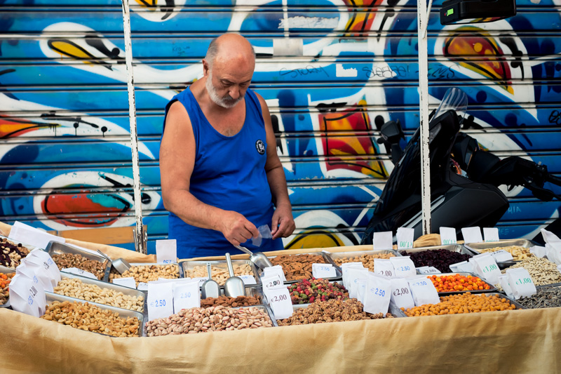 A nut and snack vendor working at a colorful market stall in Athens, Greece with graphic shutter backdrop
